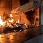 hand throwing log into burning fireplace