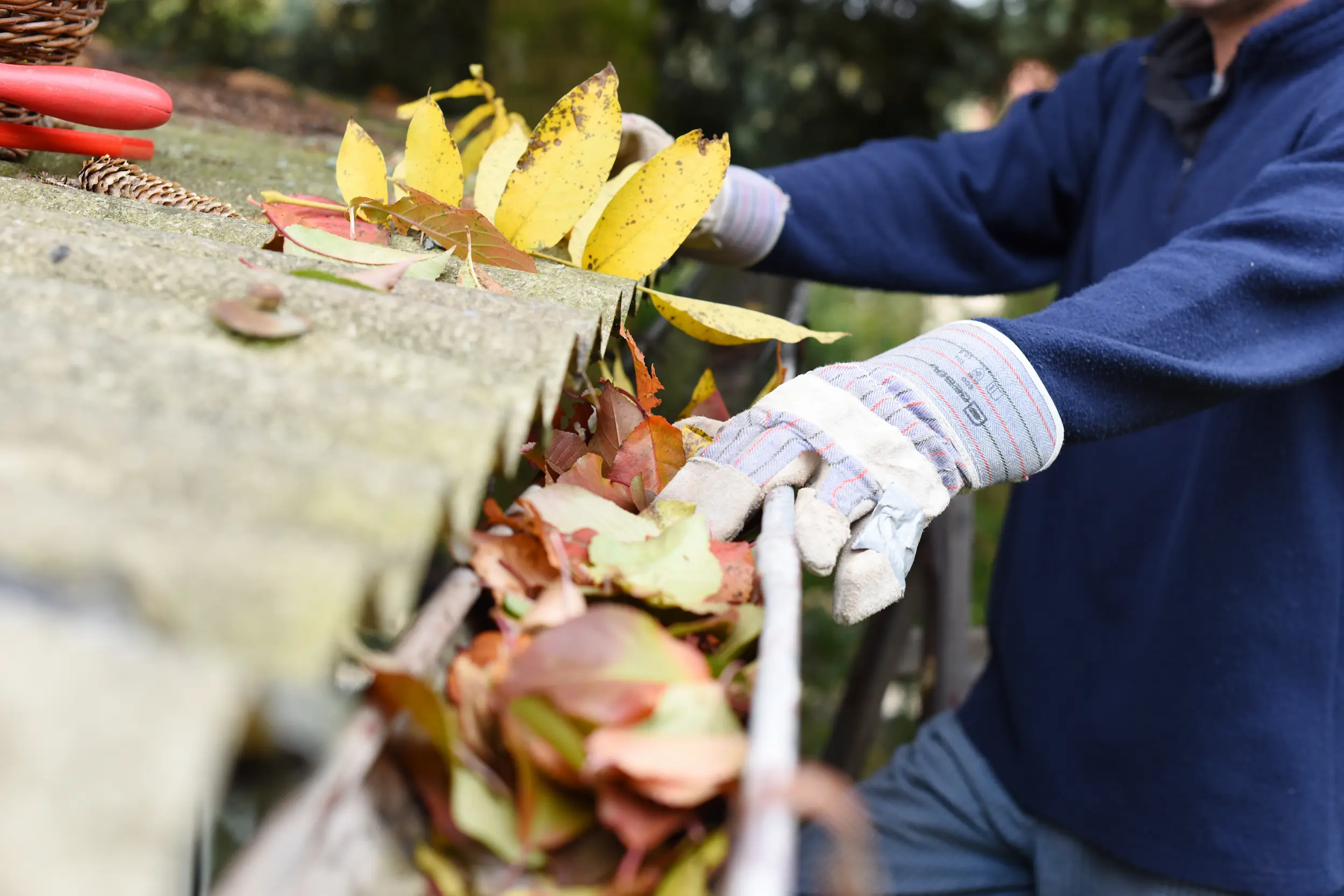 A worker cleaning leaves and debris from a home's gutter system.